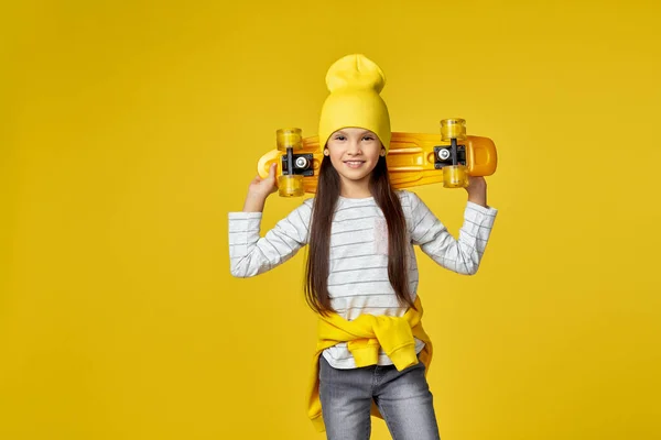 Девочка в шляпе и солнцезащитных очках с желтым скейтбордом — стоковое фото