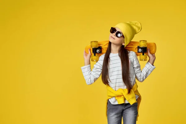 Barn flicka i hatt och solglasögon med gul skateboard — Stockfoto