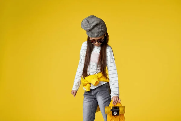 Menina em chapéu e óculos de sol com skate amarelo — Fotografia de Stock