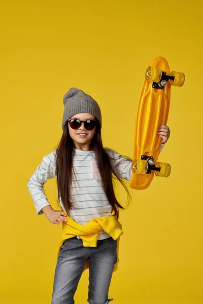 Bambina in cappello e occhiali da sole con skateboard giallo — Foto Stock