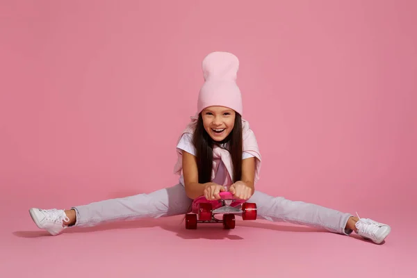 Девочка смеется и сидит на розовом скейтборде — стоковое фото