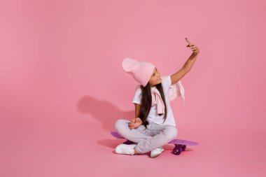 Kaykayın üzerinde oturan ve selfie çeken bir çocuk.