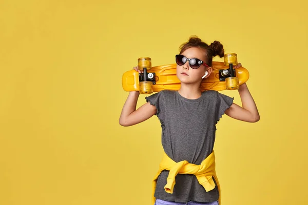 Enfant fille en lunettes de soleil posant avec skateboard jaune — Photo