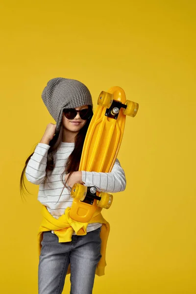 Enfant fille en chapeau et lunettes de soleil avec skateboard jaune — Photo