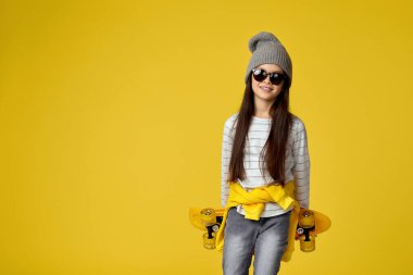 Sarı kaykaylı, şapkalı ve güneş gözlüklü çocuk.