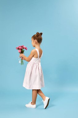 Sevimli, gülümseyen küçük kız elinde bir buket gül tutuyor.