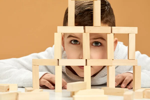 children plays with wooden constructor on desk.