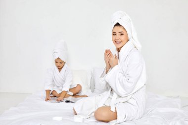 Beyaz bornozlu ve havlulu anne ellerine krem sürüyor.