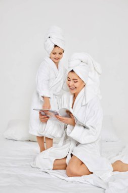 Annesi ve beyaz bornozlu kızı dergi okuyorlar.