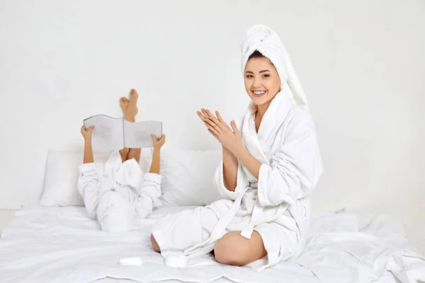 Matka v bílých županech a ručníky naneste krém na ruce — Stock fotografie