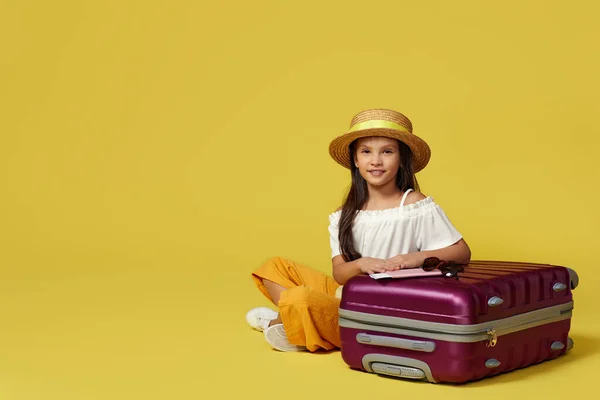 Маленька дівчинка з валізою і паспортом сидить на підлозі — стокове фото