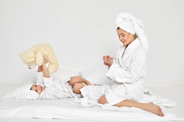 Anne manikür yapıyor ve kız da oyuncak ayıyla oynuyor.