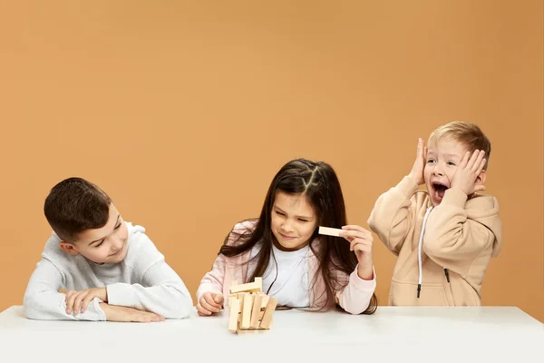 children plays with wooden constructor on desk.