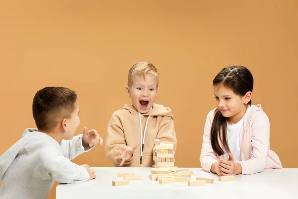 children plays with wooden constructor on desk.