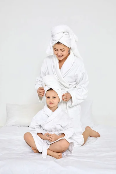 Beautiful mother and daughter in white bathrobes and towels — Stock Photo, Image