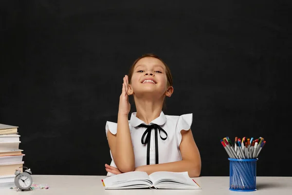 Gelukkig schoolmeisje opgeheven haar hand omhoog terwijl zitten aan tafel — Stockfoto