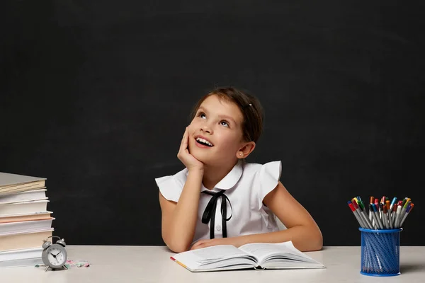 Счастливая школьница, мечтающая и сидящая за столом — стоковое фото
