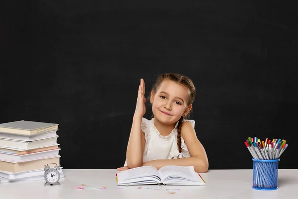 Gelukkig schoolmeisje opgeheven haar hand omhoog terwijl zitten aan tafel — Stockfoto