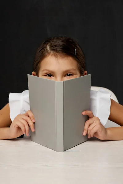 Menina criança cobrir seu rosto pelo livro — Fotografia de Stock