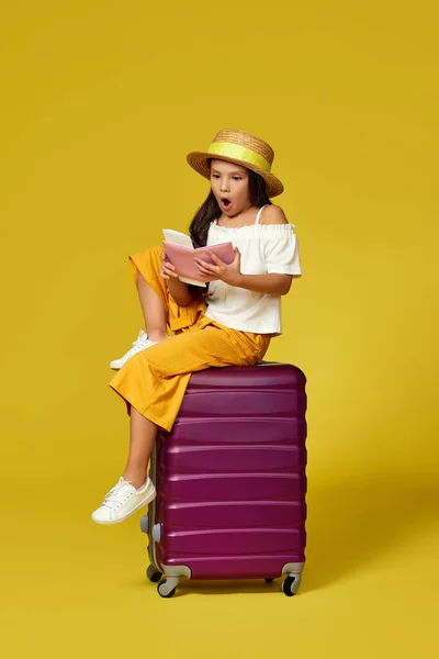 Дитяча дівчина в капелюсі з паспортом і квитком, що сидить на валізі — стокове фото