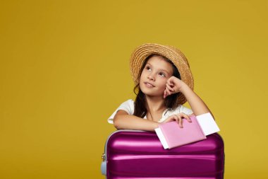 Sarı arka planda pembe valizli çocuk.