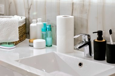 Lavabo lavabosu, musluğu ve kozmetik şişeleri olan banyo.
