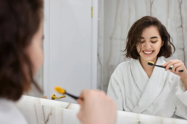 Mujer en batas blancas cepillándose los dientes delante del espejo — Foto de Stock