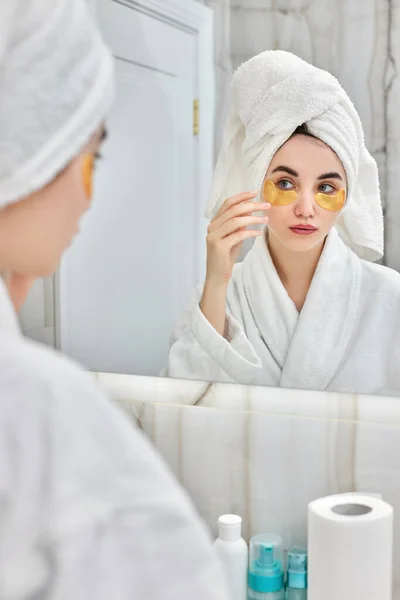 Schöne Frau mit Augenklappen in weißen Bademänteln im Badezimmer — Stockfoto