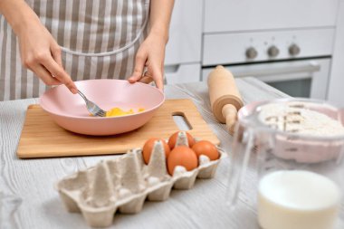 Kadın kasede yumurta çırpıyor. Ev hanımı mutfakta yemek yapıyor.