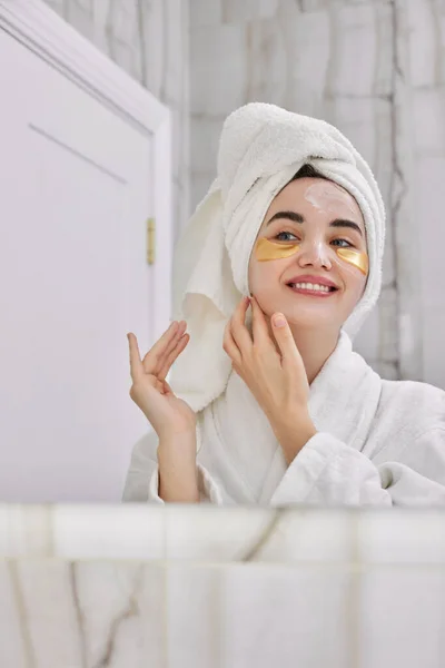 Beautiful woman with eye patches in white bathrobes in bathroom — Stock Photo, Image