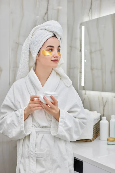 Beautiful woman with eye patches in white bathrobes in bathroom — Stock Photo, Image