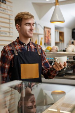 Önlüklü erkek garson elinde bir bardak sıcak içecek tutuyor.