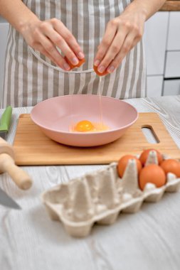 Kadın kasede yumurta kırıyor. Ev hanımı mutfakta yemek yapıyor.