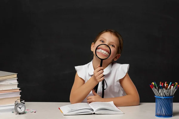 Симпатичная счастливая школьница, выглядывающая через лупу — стоковое фото