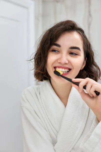 Mulher em roupões de banho brancos escovando os dentes na frente do espelho — Fotografia de Stock