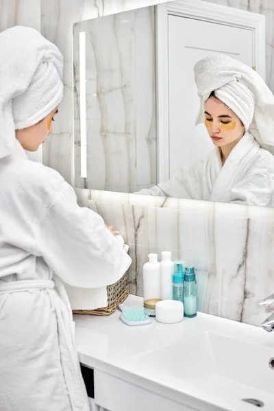 Hermosa mujer con parches para los ojos en albornoces blancos en el baño — Foto de Stock