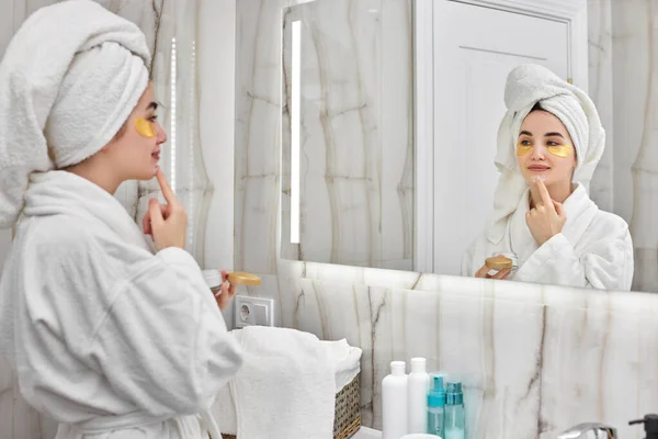Hermosa mujer con parches para los ojos en albornoces blancos en el baño — Foto de Stock