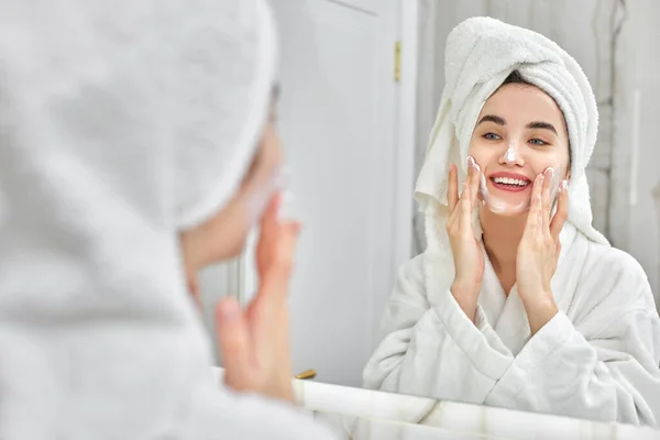 Mujer en batas blancas aplicando aplicar crema facial — Foto de Stock