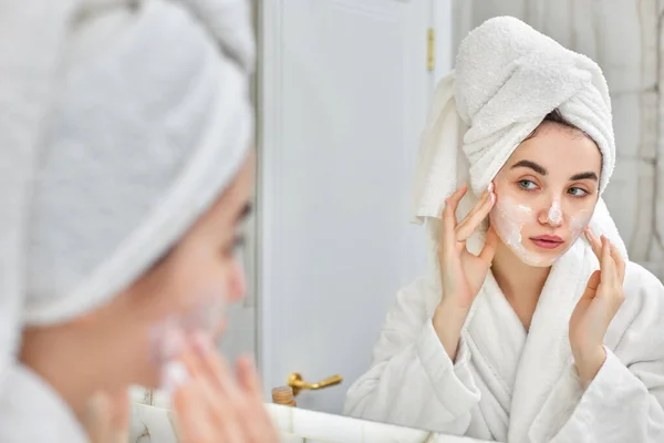 Frau in weißen Bademänteln trägt Gesichtscreme auf — Stockfoto