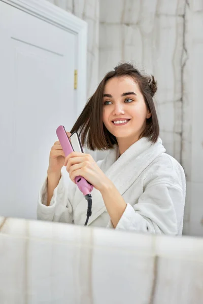 Nő használ hajvasaló a fürdőszobában. — Stock Fotó