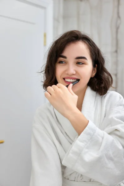 Frau in weißen Bademänteln beim Zähneputzen vor Spiegel — Stockfoto