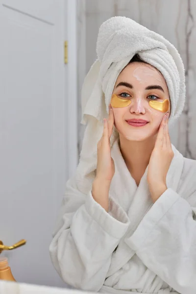 Mulher bonita com manchas nos olhos em roupões de banho brancos no banheiro — Fotografia de Stock