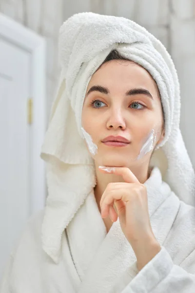 Woman in white bathrobes applying apply facial cream — Stock Photo, Image