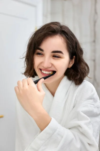 Frau in weißen Bademänteln beim Zähneputzen vor Spiegel — Stockfoto