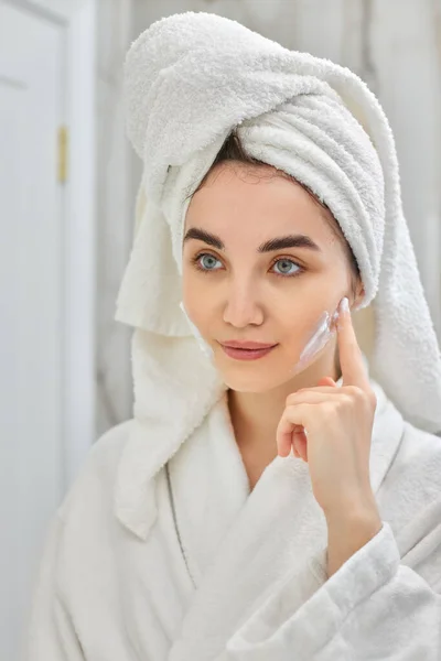 Mujer en batas blancas aplicando aplicar crema facial — Foto de Stock