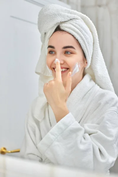 Mujer en batas blancas aplicando aplicar crema facial — Foto de Stock