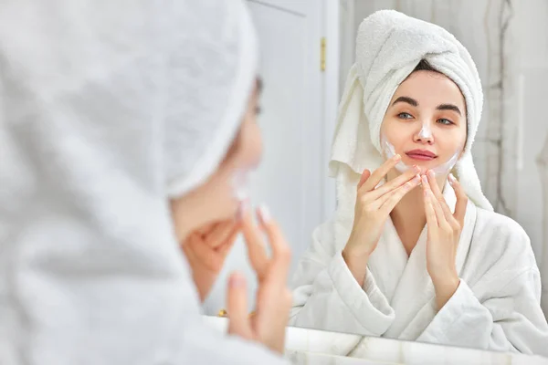 Mujer en batas blancas aplicando aplicar crema facial — Foto de Stock