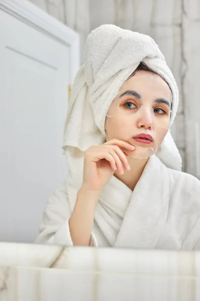 Vrouw in wit badjas in de voorkant van spiegel in badkamer — Stockfoto