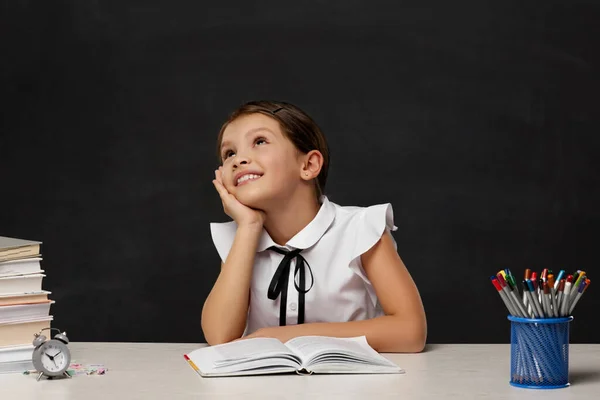 Gelukkig schoolmeisje dagdromen en zitten aan tafel — Stockfoto