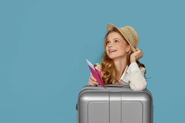 Усміхнена блондинка з сірою валізою, паспорт — стокове фото